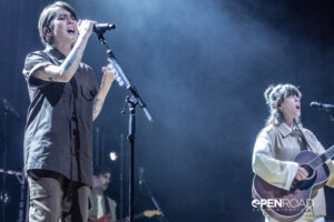 Tegan and Sara sing on stage bathed in blue lighting